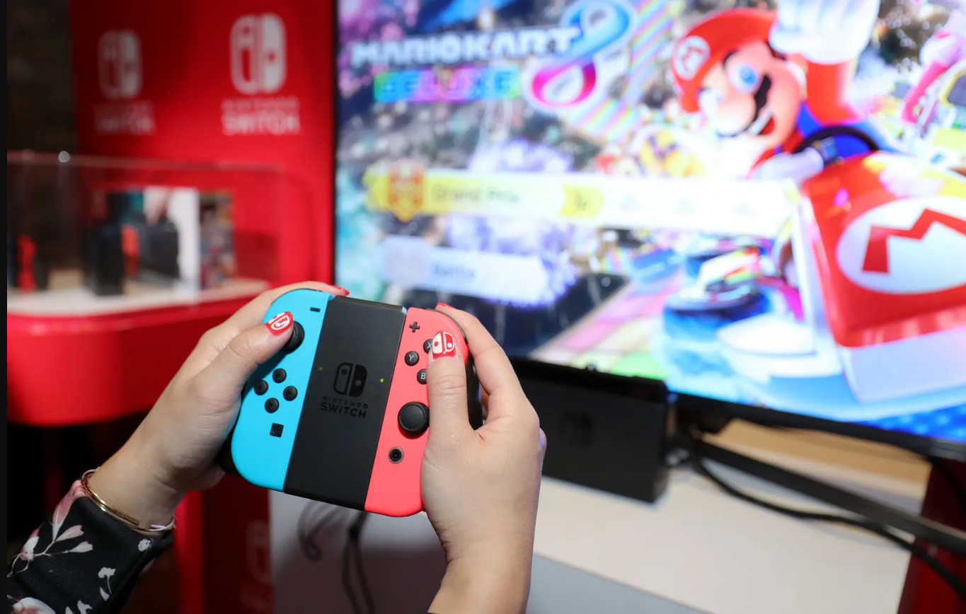 Hands holding a Nintendo Switch controller as they play Mario Kart