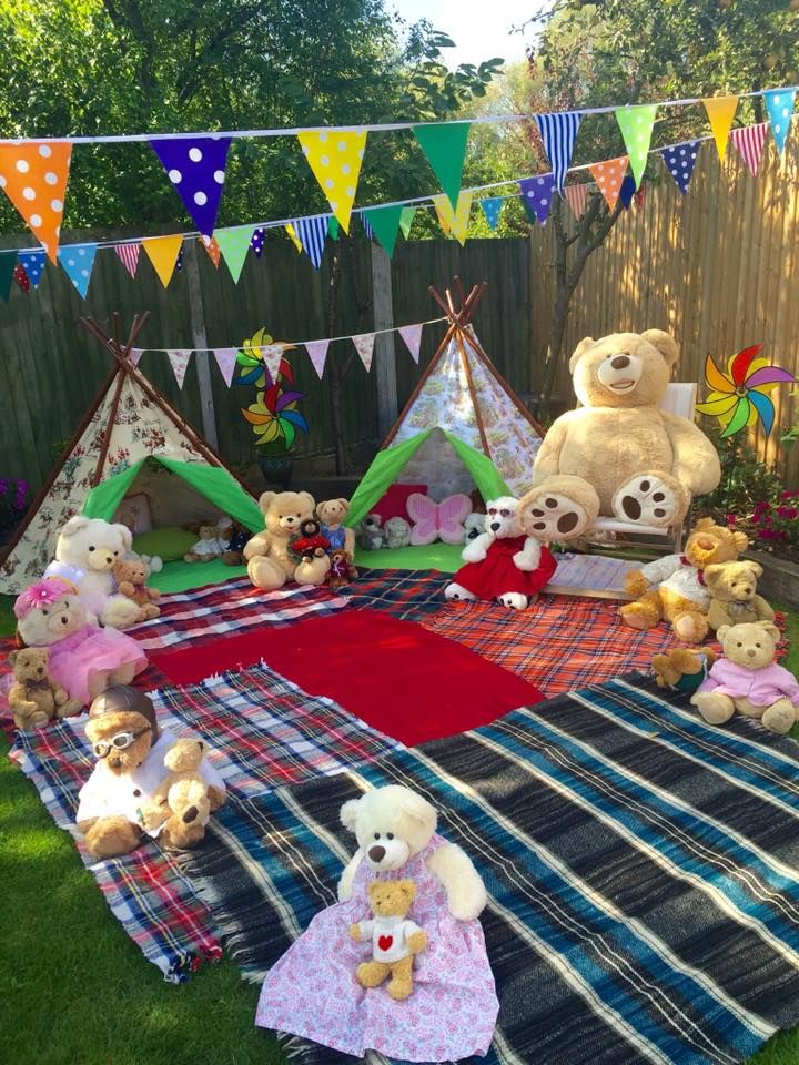 image of stuffed animals sitting on a plaid blanket under the trees having a picnic
